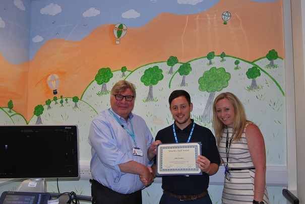 Ben Sinden receives his award from Trust Chairman David Clayton-Smith in front of his artwork along with Dr Jenny Dagiakidi Consultant Radiologist