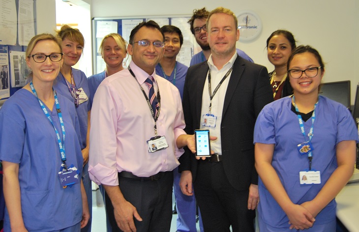 Professor Nikhil Patel Consultant Cardiologist holding smartphone with Dr Richard Veasey Consultant Cardiologist with some of the Cardiology team