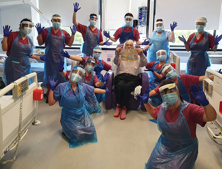 Back row - left to right Denise De La Cruz (Nurse), David Batchelor (Clinical Orderly), Andrew Aslett (HCA), Dimitris Raptis (HCA), Katie Pettet (HCA), Lita (Ward Housekeeper). Left side of patient Jon McMullon crouching, back to front: Stefana Sandu (HCA), Carol Stonestreet (SN), Mollie Taylor (Sister) Right side of Jon crouching, back to front: Martina Barry (SN), Kate Bridgett (SN), Cheryl Baxter (Ward Matron)