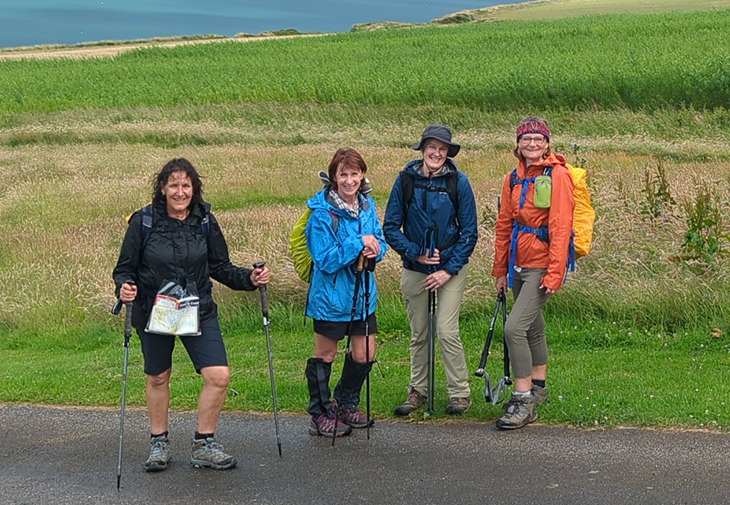 four people walking on hills with sea on the background