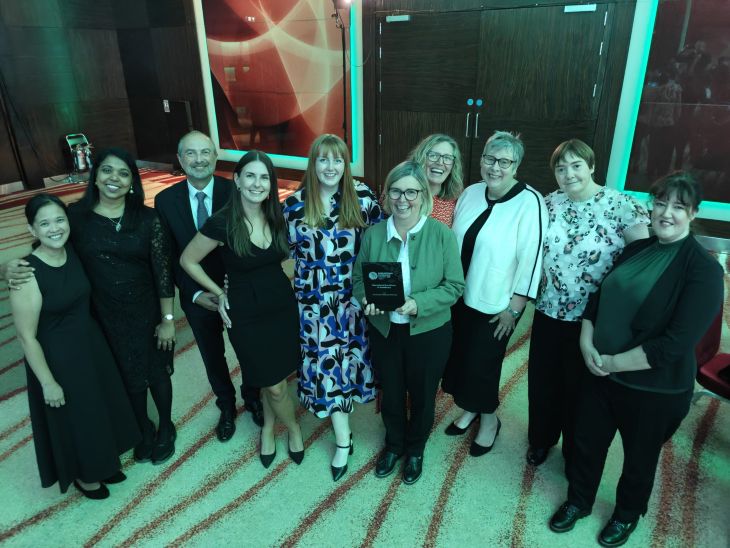 A group of people standing in a line, smiling as they hold an award. 