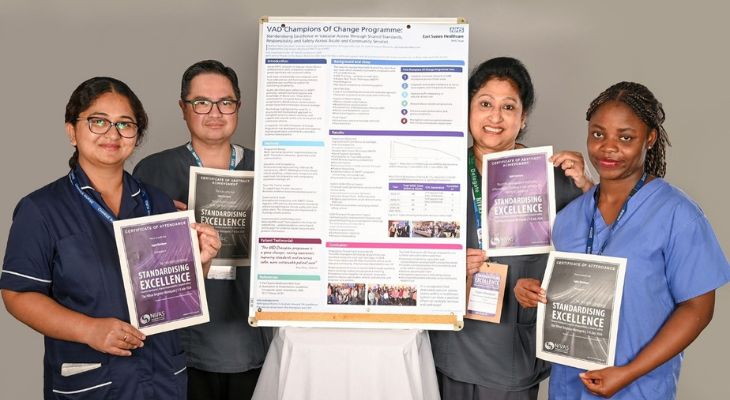 A group of four people stand smiling around an informational poster.