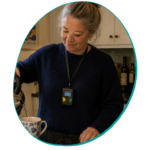 Photo of a woman making a cup of tea whilst wearing a lanyard around her neck which has a small device on it monitoring her heart.