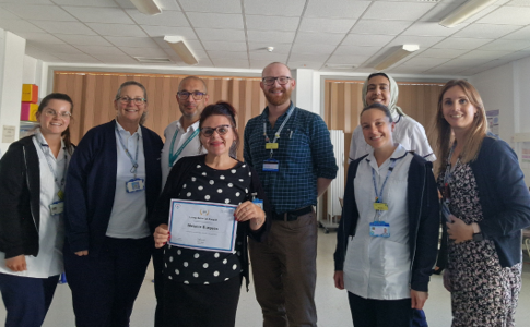 A group of people standing together in a clinical setting. One in the middle holds a certificate.